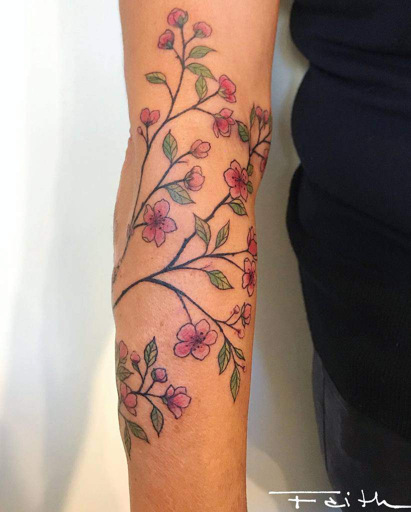 Arm tattoo of a blossoming branch adorned with pink flowers and lush green leaves