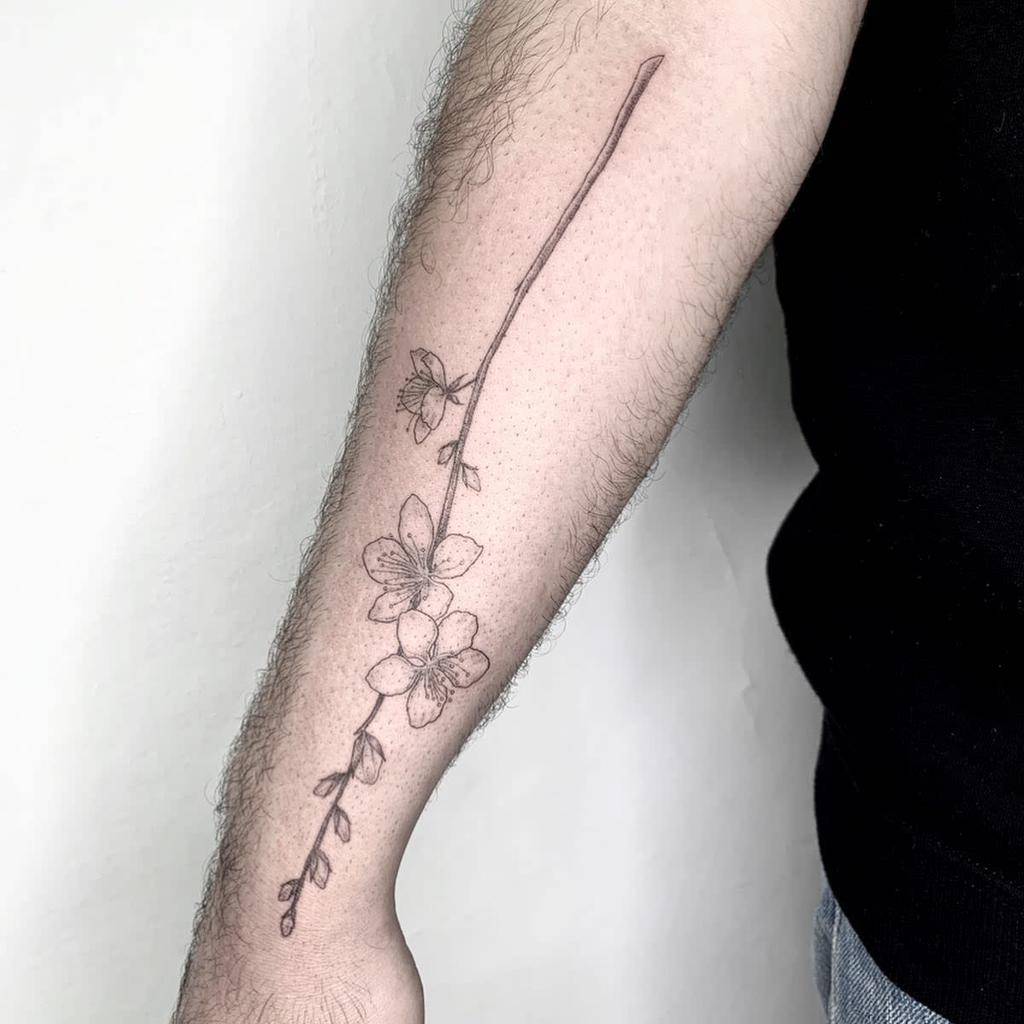 A delicate flower tattoo, intertwined with a graceful branch, extends from the wrist towards the elbow on the person's forearm