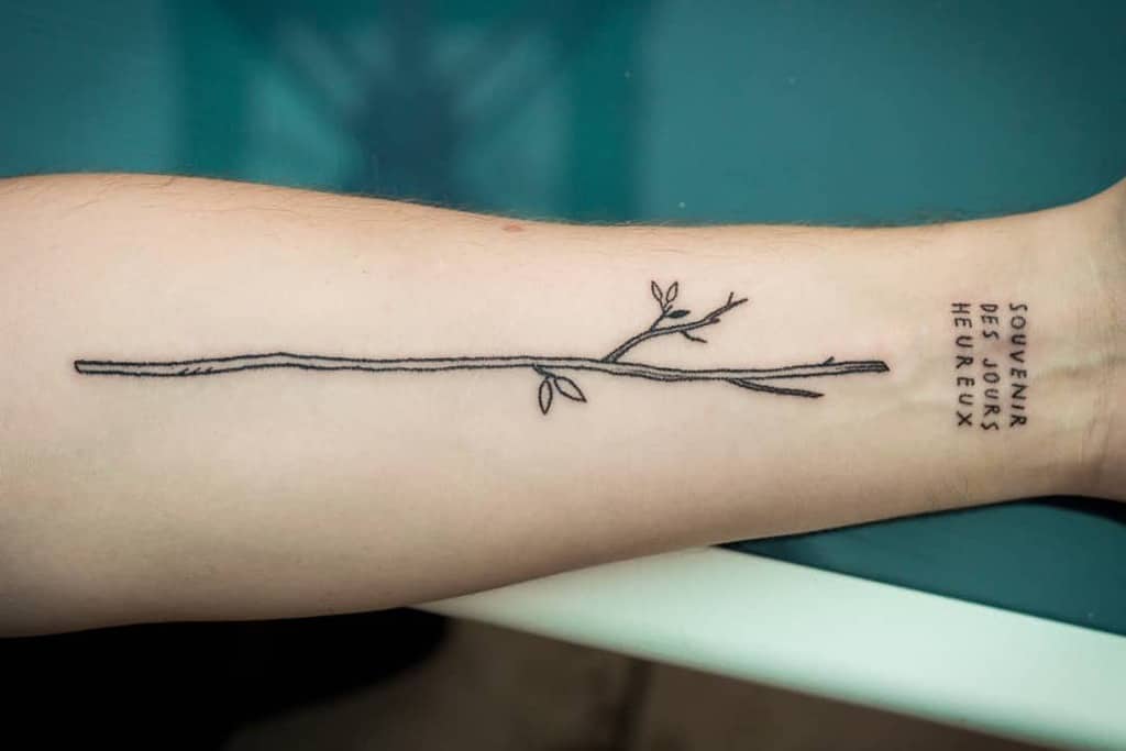 Minimalist branch tattoo on forearm, with French text beside it