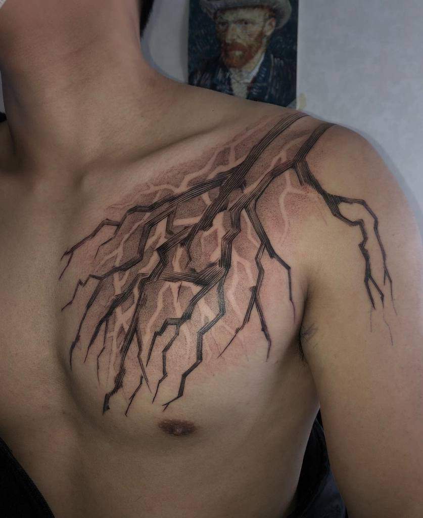 Black ink tree branch tattoo elegantly sprawls across a person's chest and shoulder, showcasing intricate details and delicate shading