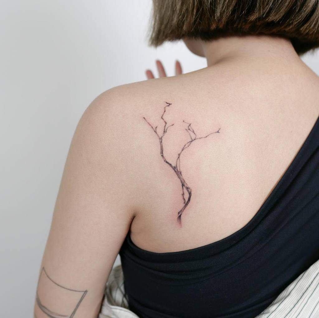 A person with short hair showcases a tattoo of a branch on their upper back