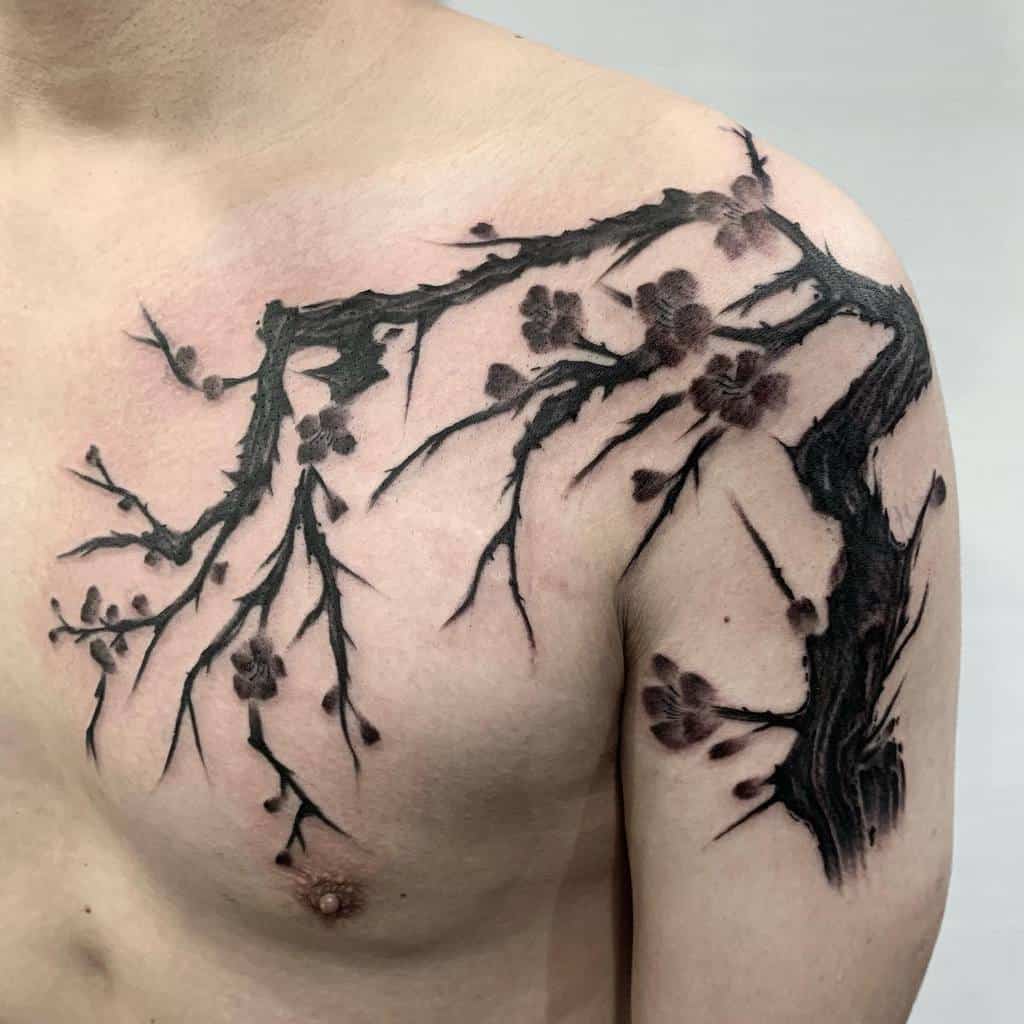 Tattoo of a dark tree branch with subtle blossoms, spreading across the shoulder and upper chest in bold, black ink