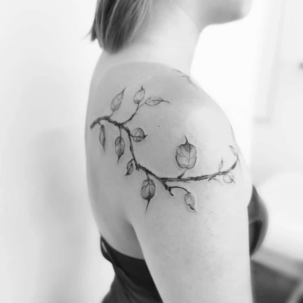 Black and grey tattoo of a delicate tree branch with leaves, wrapping around the shoulder and upper arm