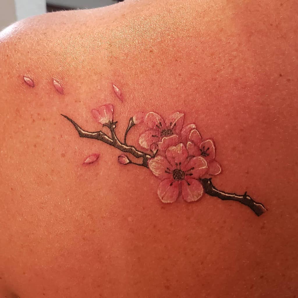 A branch with pink cherry blossoms tattooed on a shoulder