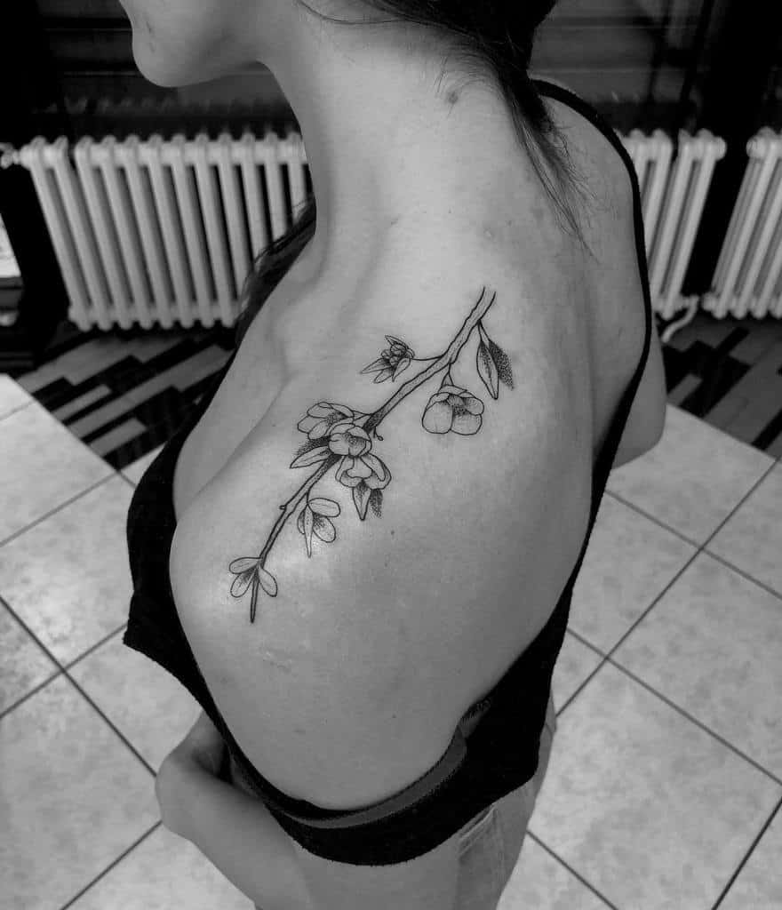 Black and white tattoo of a flower branch gracefully extending across a person's upper back and shoulder