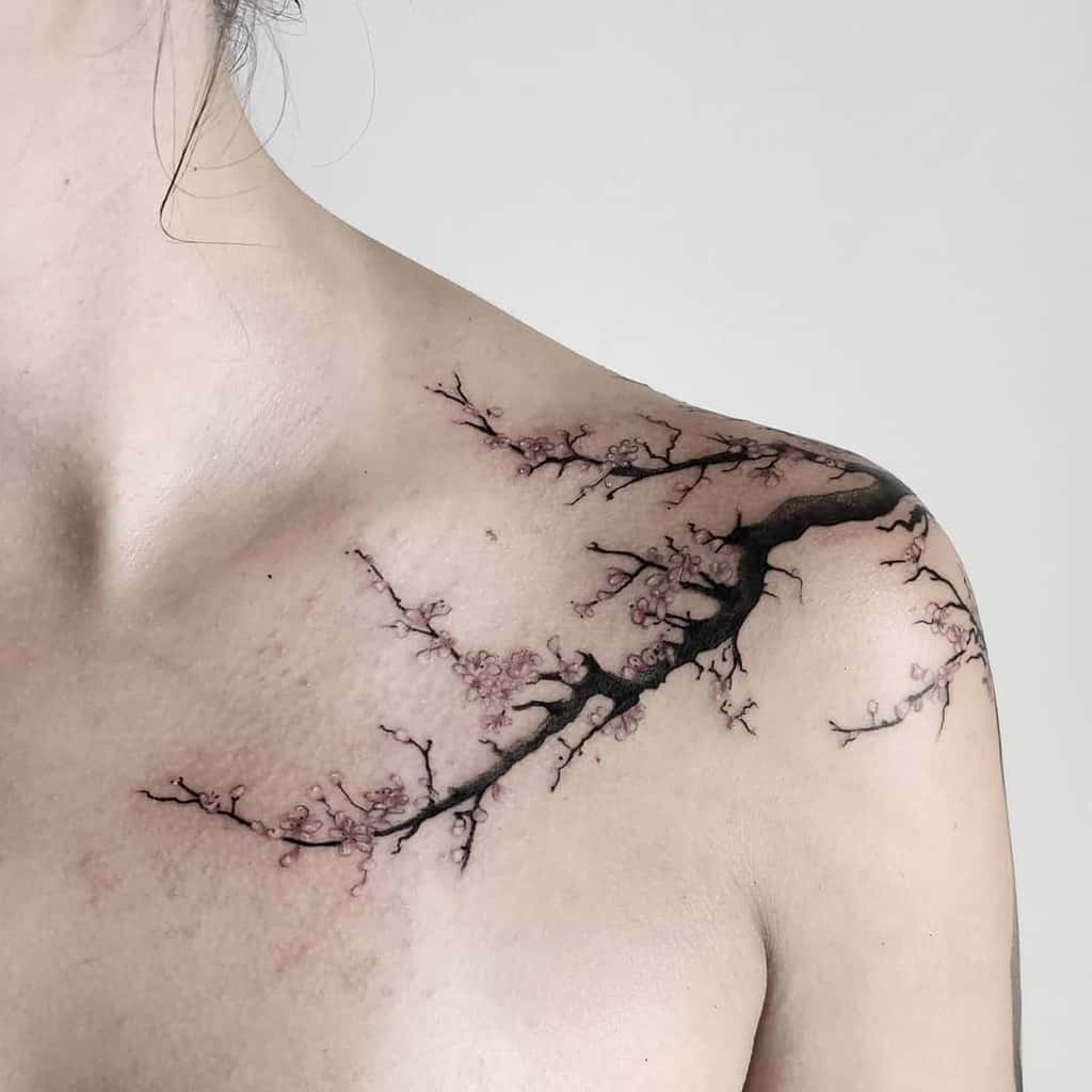Delicate cherry blossom tattoo extending from a branch on the collarbone to the upper arm on a person's shoulder