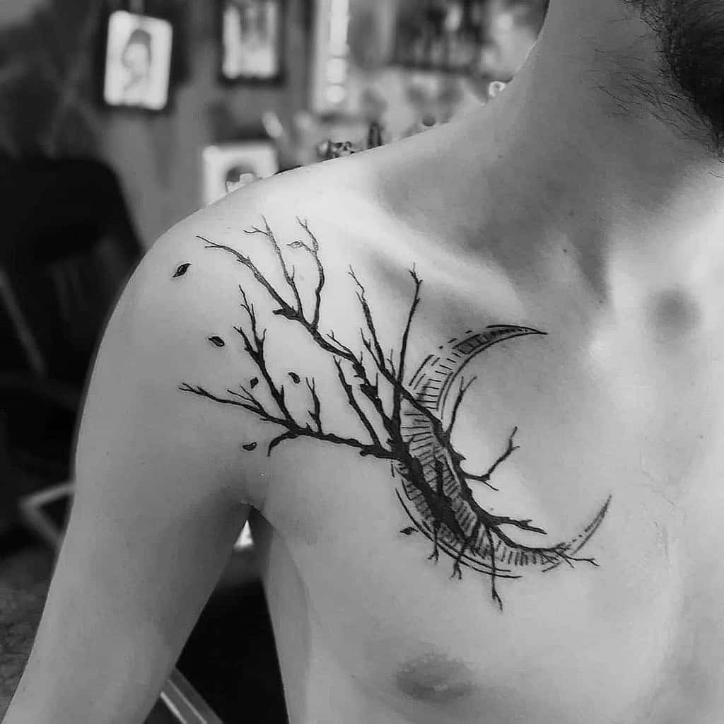 Black ink tattoo of intertwining branches with a crescent moon, elegantly etched on a person's upper chest and shoulder