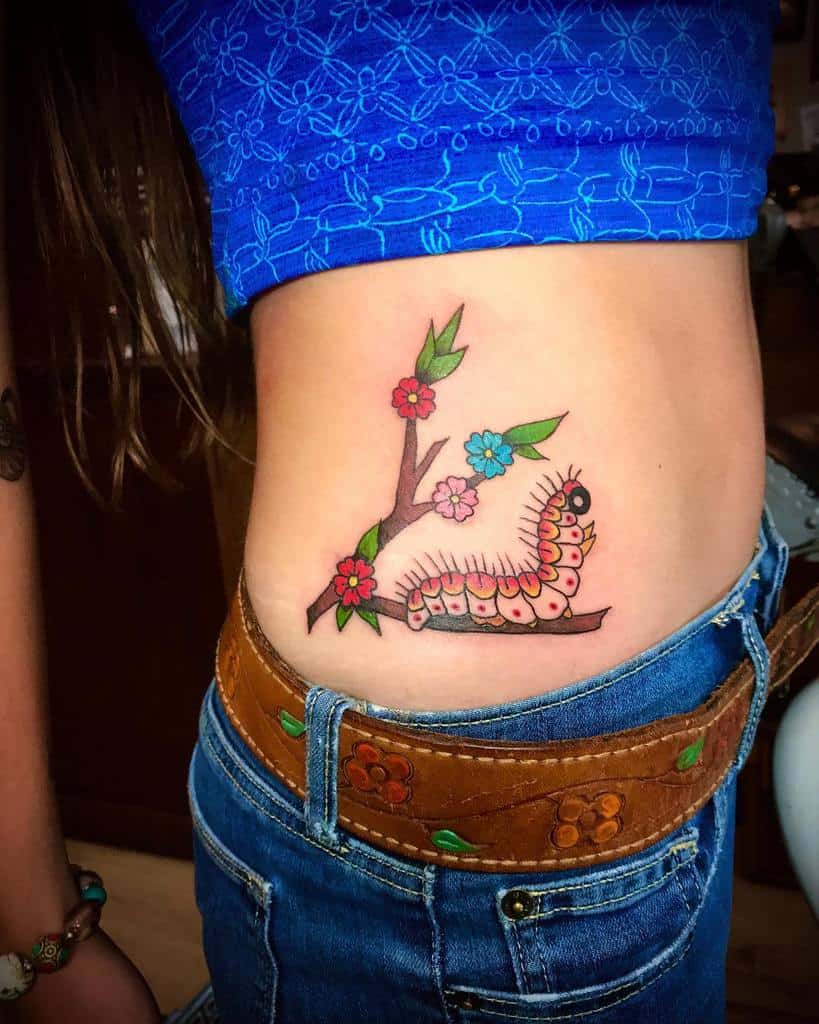 Colorful tattoo of a branch with vibrant flowers and a playful, detailed caterpillar, placed on the side of the torso