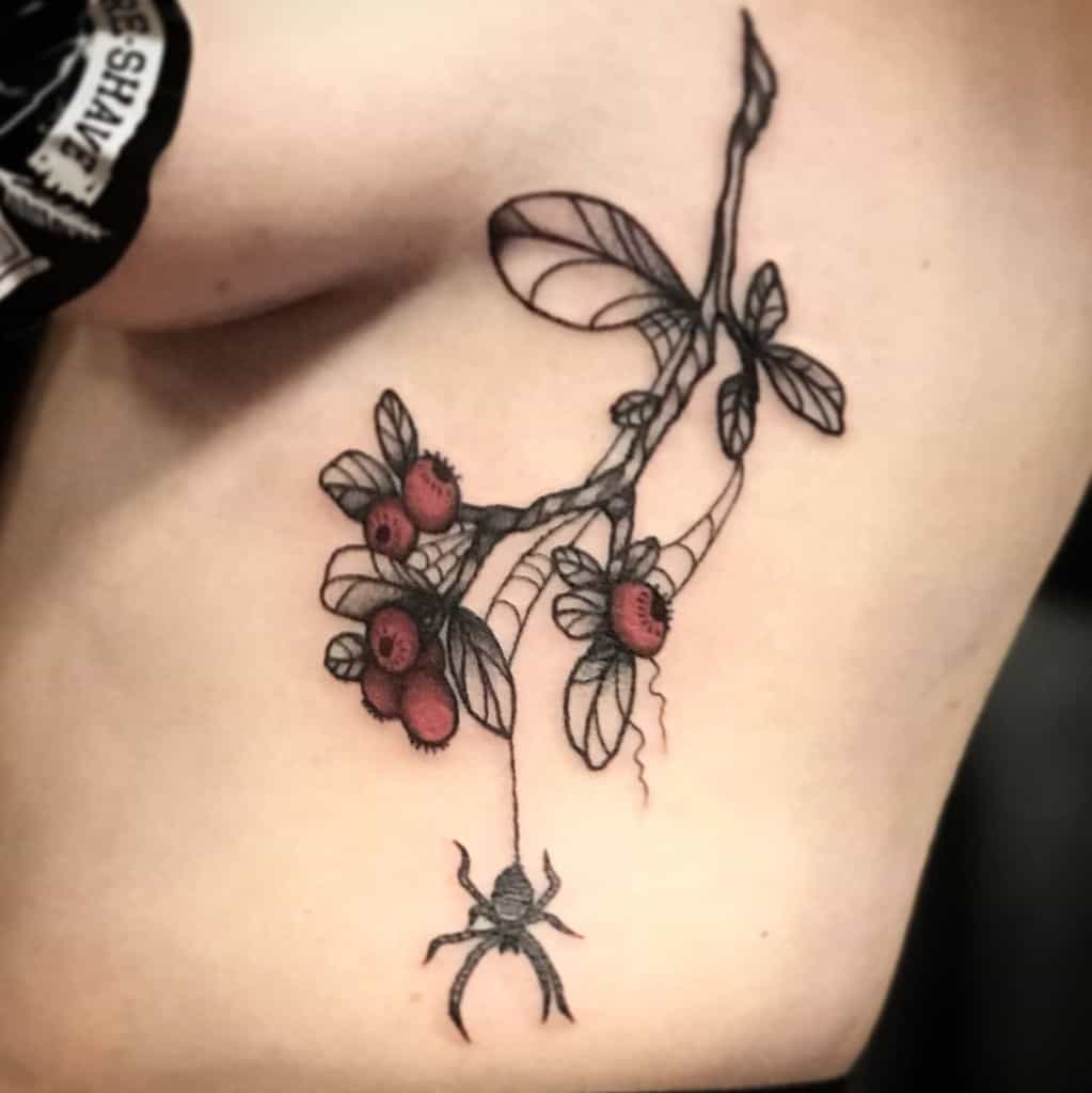 Tattoo of berries on a branch with a spider dangling from a web