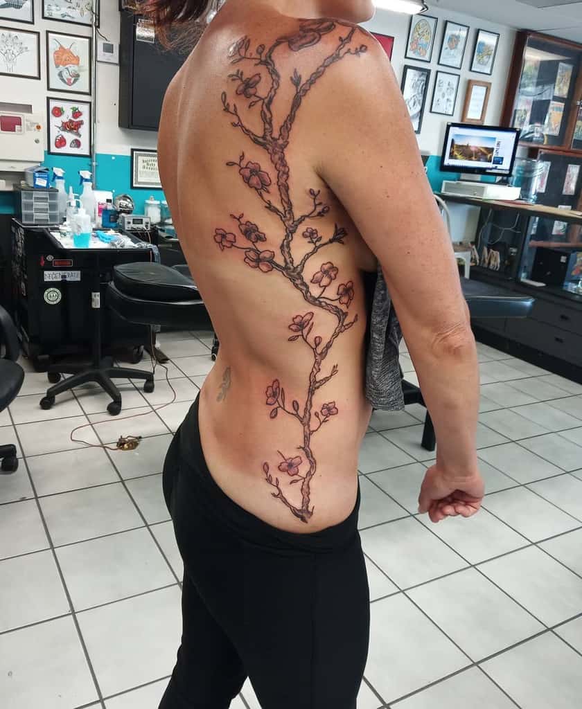 A woman with a large, detailed cherry blossom tree tattoo, its elegant branches extending across her back and side