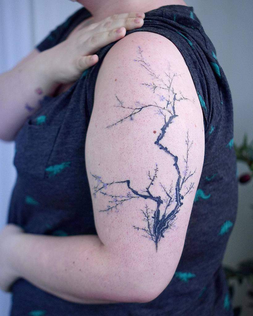 Delicate black ink tattoo of a minimalistic tree branch with fine, intricate details, creating an elegant and organic design on the upper arm.