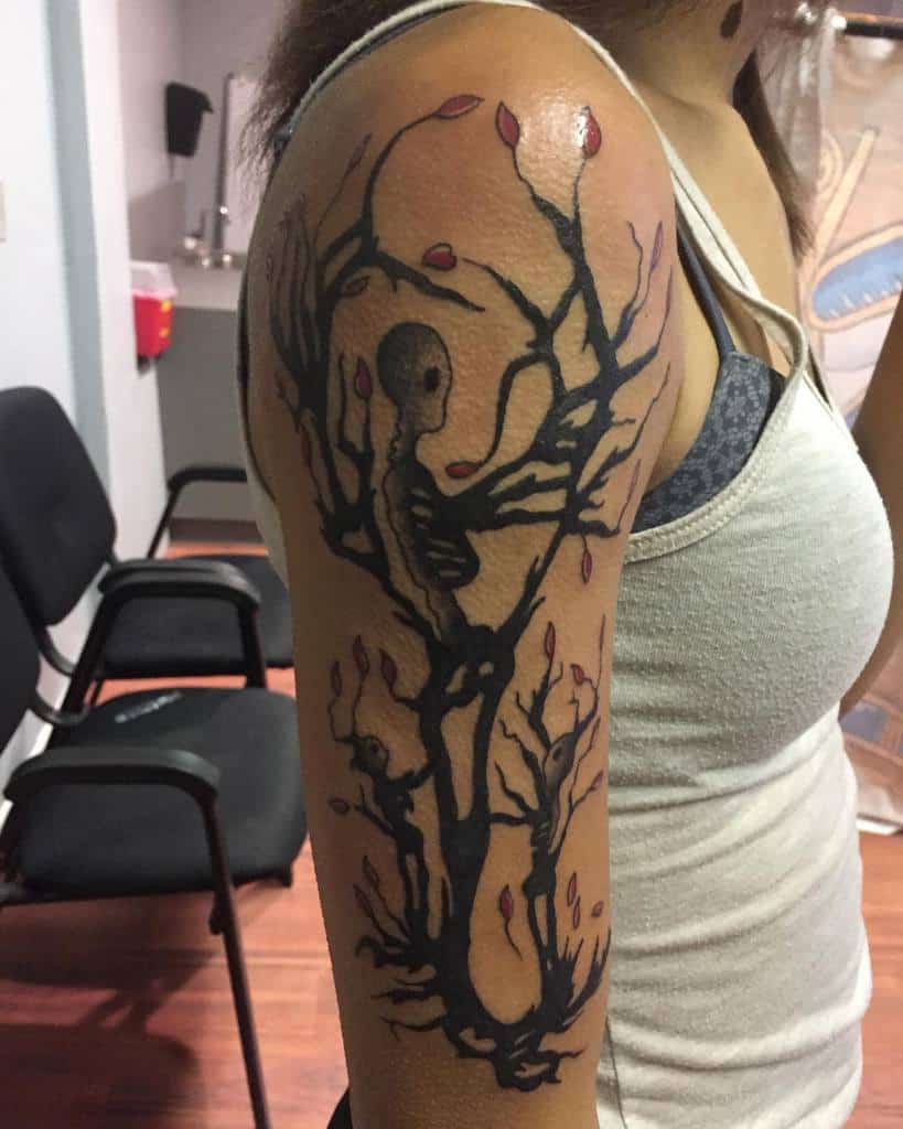 Woman with an intricate tree tattoo featuring a hidden skull among its branches on her upper arm