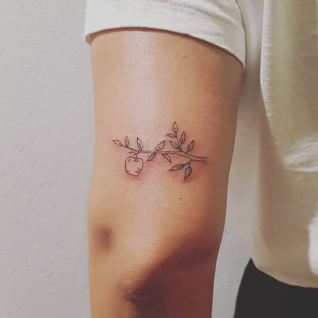 Minimalist tattoo of an apple and a delicate branch with leaves on a person's upper arm