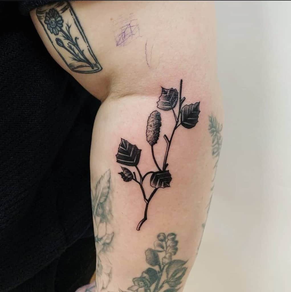 Tattoo of a bold black branch with leaves and a cone, placed on the upper arm with detailed shading and contrast