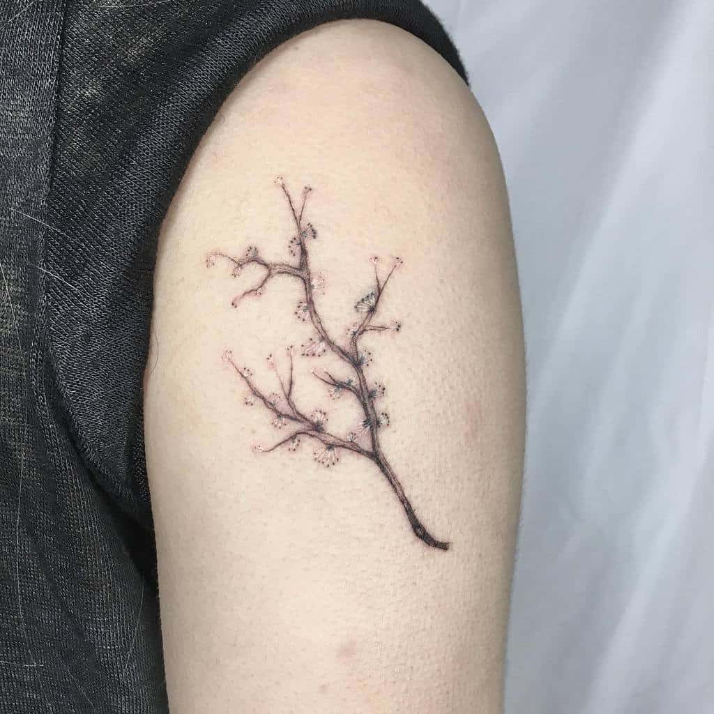 A delicate tattoo of a branch, stripped of leaves, graces the upper arm