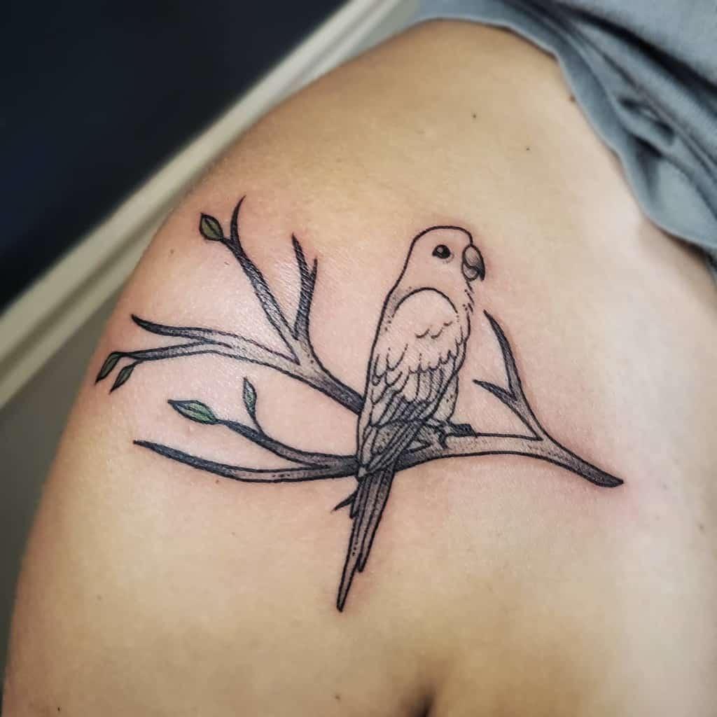 Tattoo of a parrot perched on a leafy branch adorning a person's shoulder