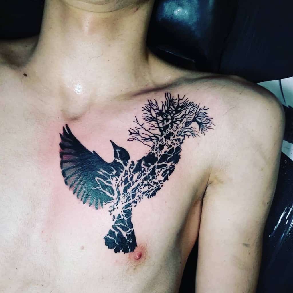 Tattoo of a bird in flight with branches integrated into its wings, positioned on the chest in bold black ink
