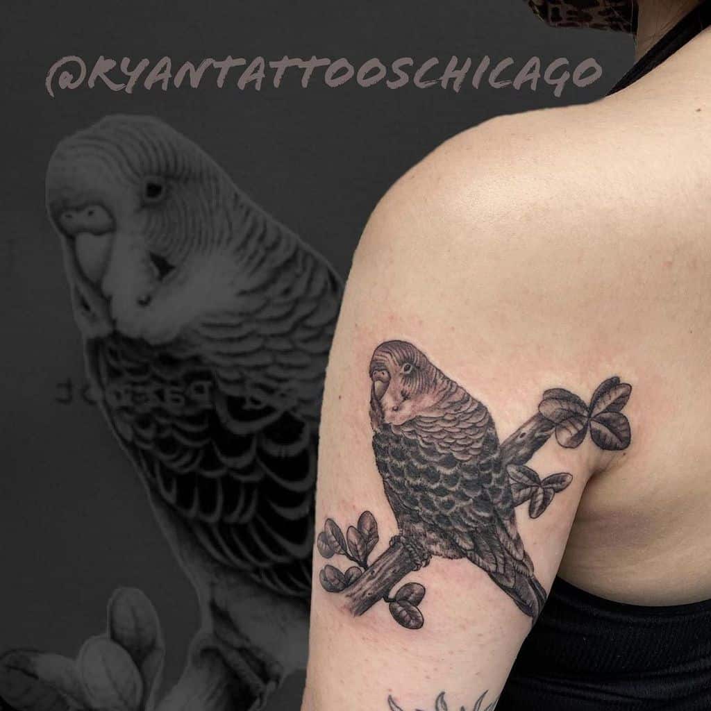 Realistic tattoo of a parrot perched on a branch, covering the upper arm with intricate shading and detailed line work