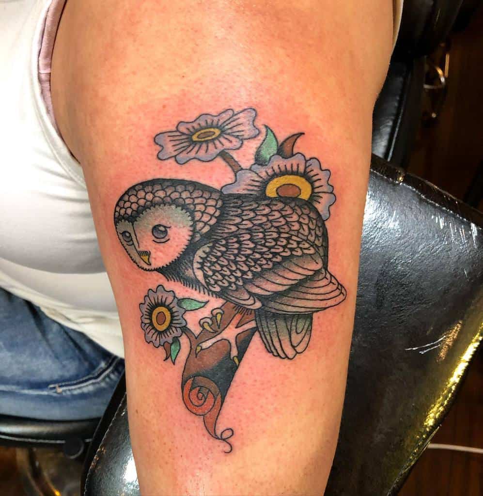 A tattoo of an owl gracefully perched on a blooming branch, beautifully placed on the upper arm