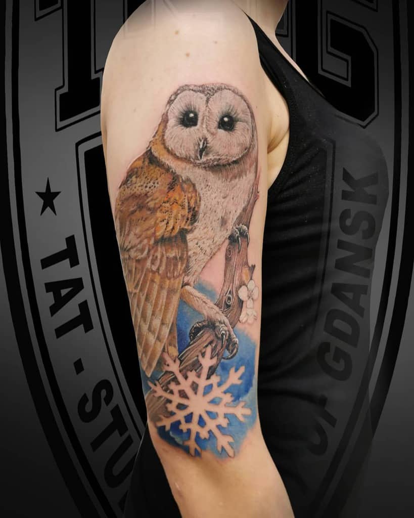 Tattoo of a barn owl perched on a beautifully detailed branch, with a snowflake delicately etched in the background on a person's upper arm