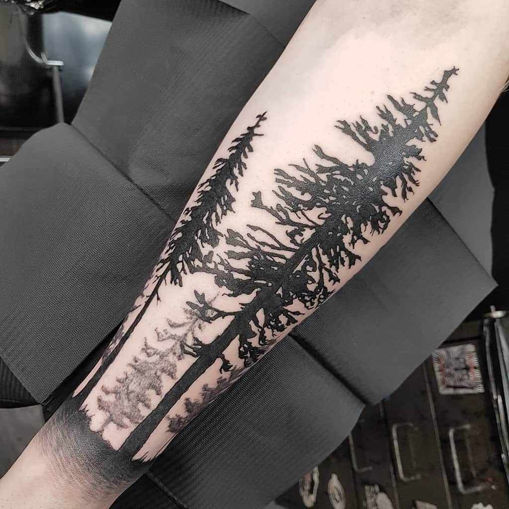 Bold tree silhouette tattoo on the forearm featuring tall, detailed evergreens, symbolizing strength, wilderness, and endurance