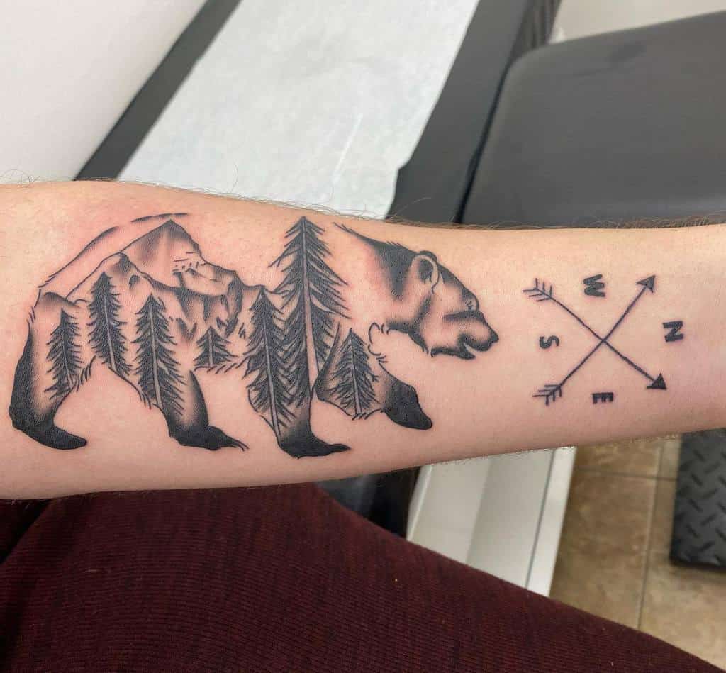 Tattoo of a bear silhouette filled with intricate trees and towering mountains, with a detailed compass design beside it