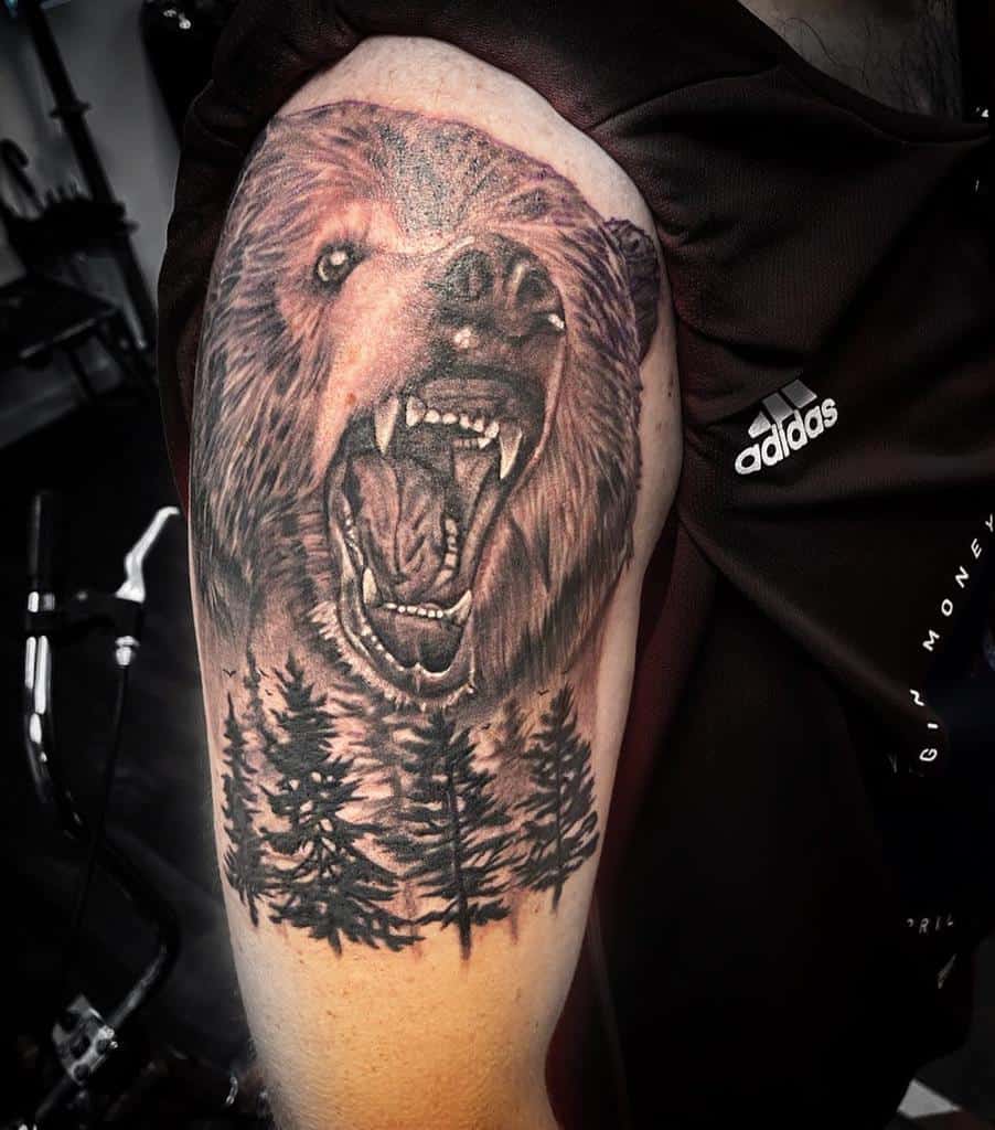Tattoo on an upper arm featuring a roaring bear and the silhouettes of trees below