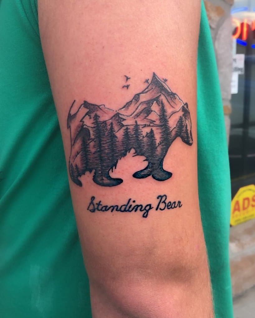 Tattoo of a bear silhouette featuring mountain and tree scenery inside, with the text "Standing Bear" below