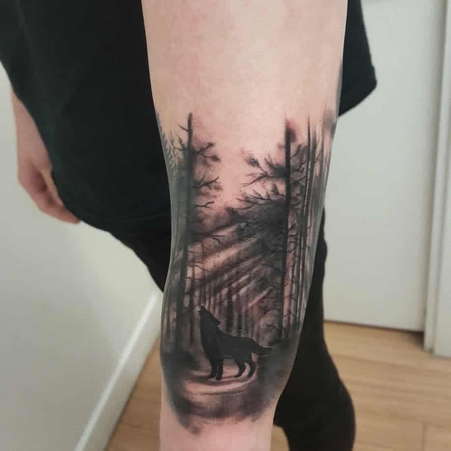 A forest tattoo featuring the silhouette of a howling wolf among the trees on a forearm