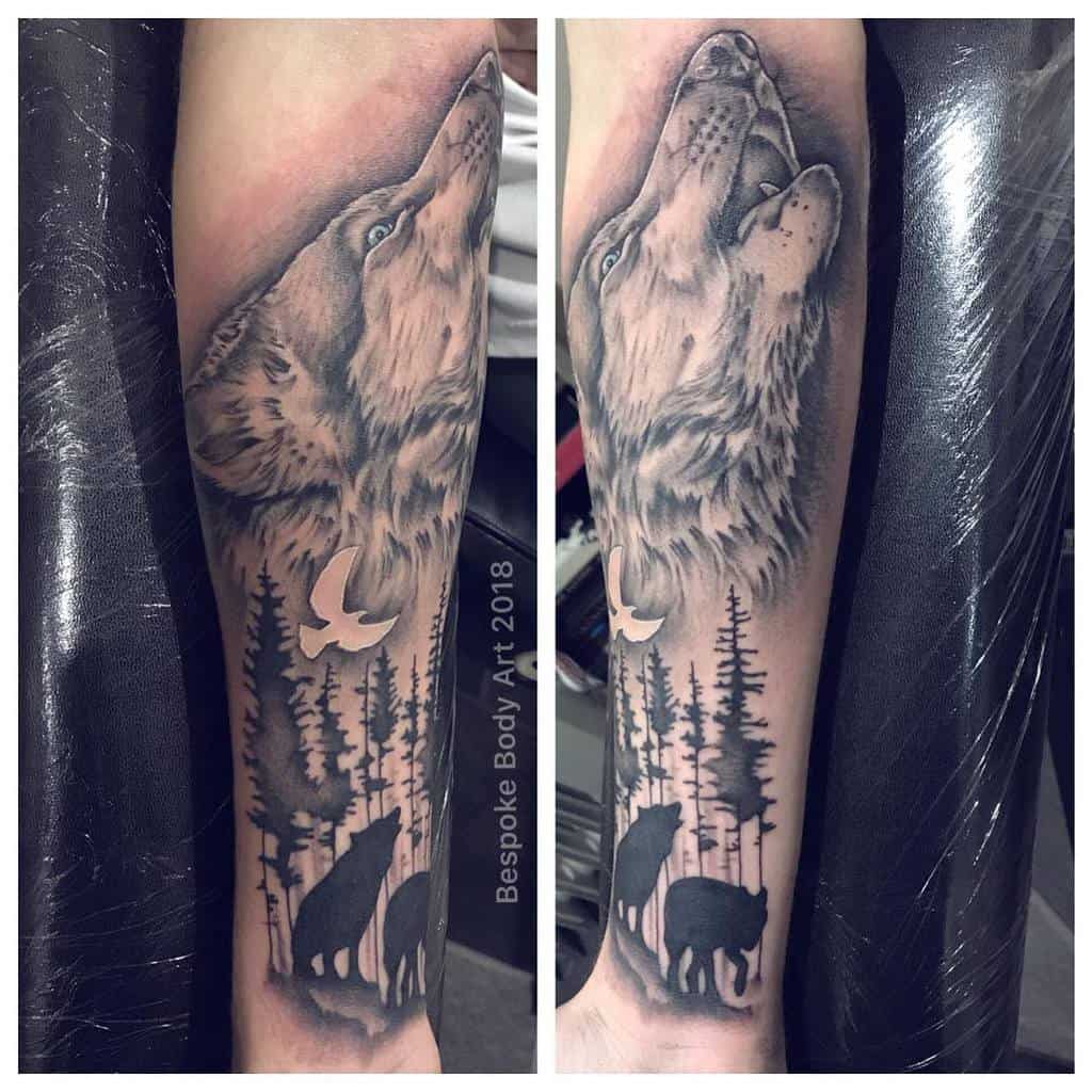 Detailed forearm tattoo featuring a howling wolf above tree silhouettes and wildlife, symbolizing freedom, nature, and unity with the wild