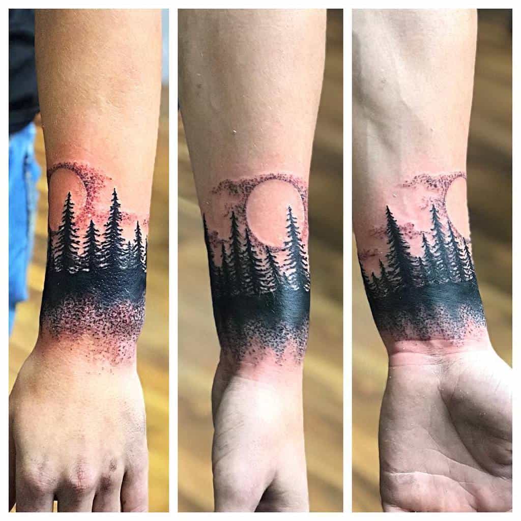 Tattoo of a forest landscape on a person’s wrist, featuring trees and a full moon