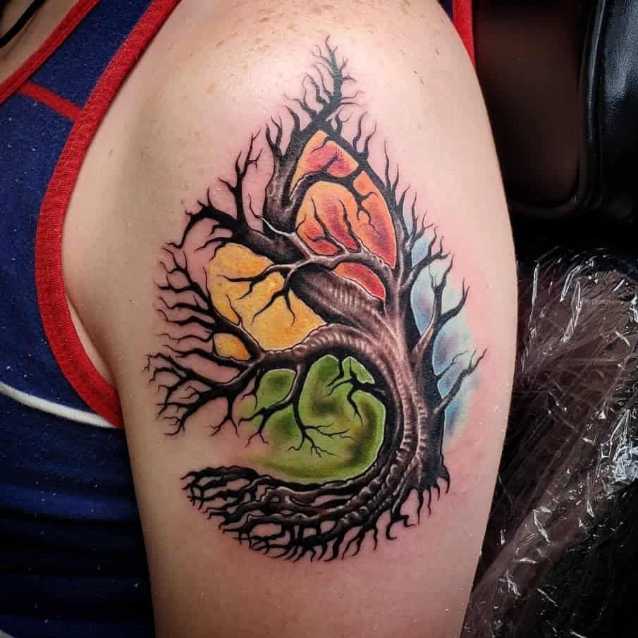 Tattoo of a colorful tree with exposed roots on a person's upper arm