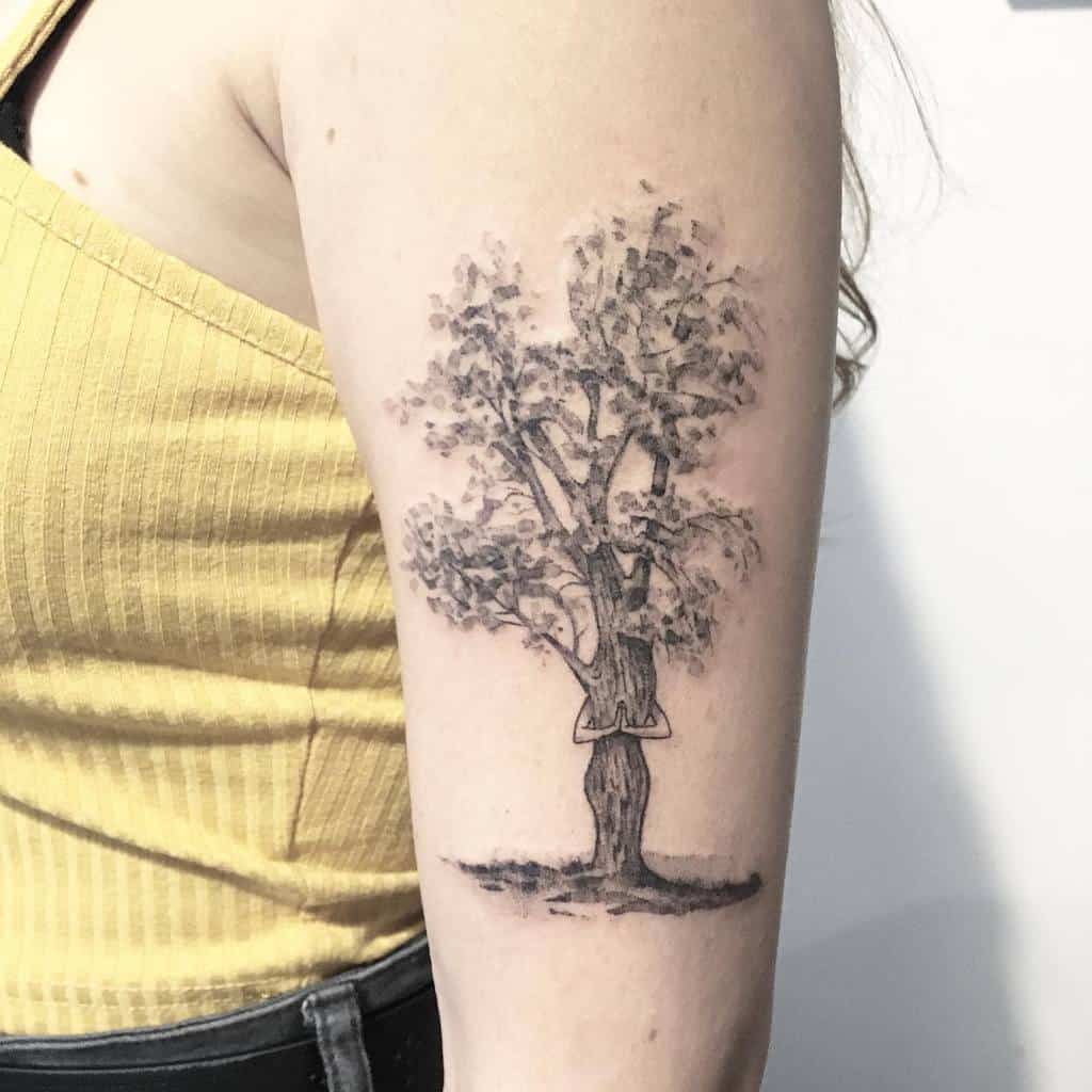Tattoo of a tree with a woman reading on one of its branches on an upper arm