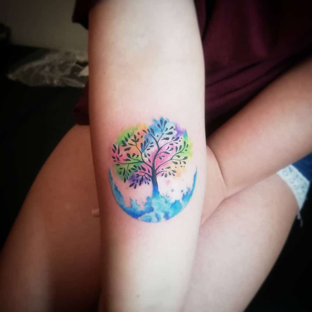 Vibrant watercolor tattoo of a tree with multicolored leaves inside a circular design, symbolizing growth, harmony, and the beauty of nature.