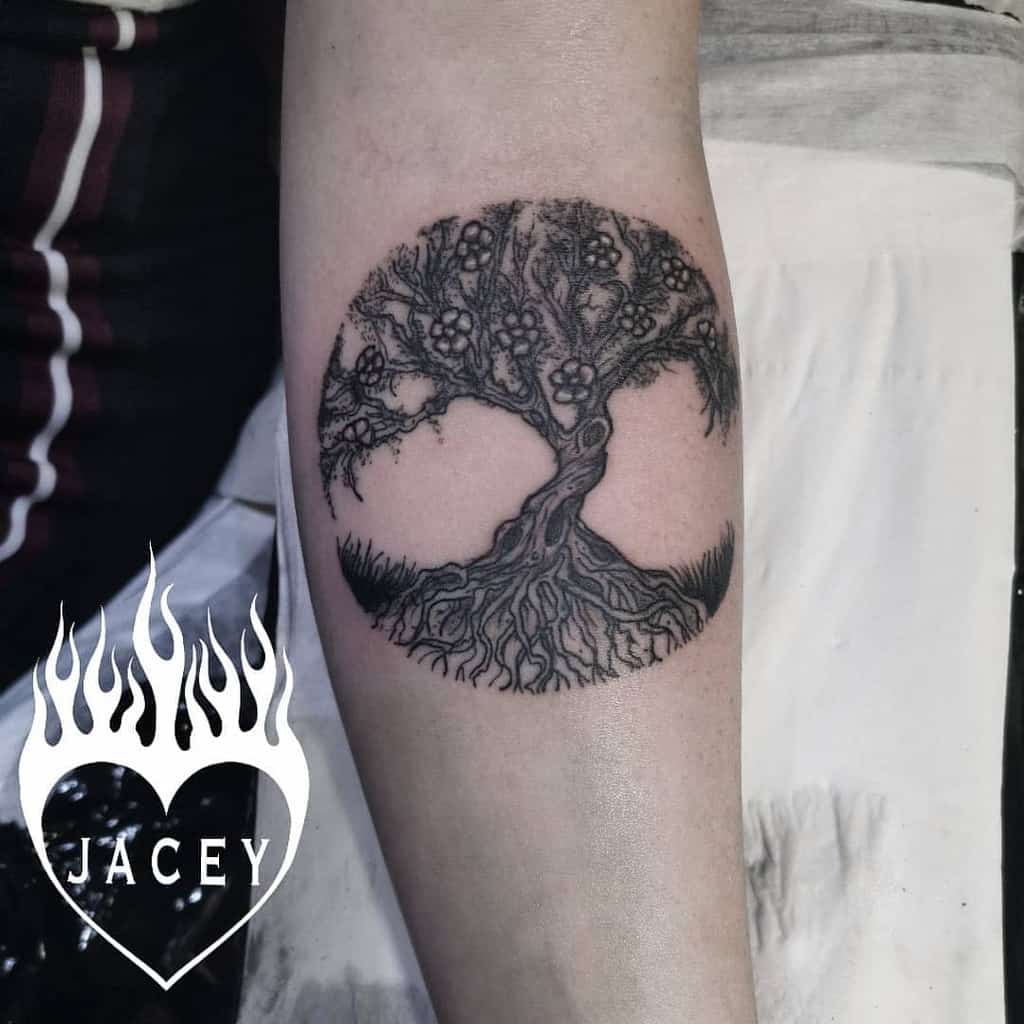 Tattoo of a tree with roots forming a yin-yang symbol on a forearm