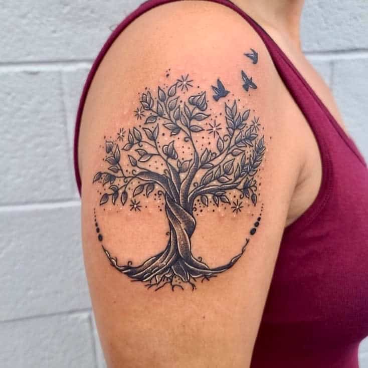 Tattoo of a tree with roots and birds flying around it on a person's upper arm