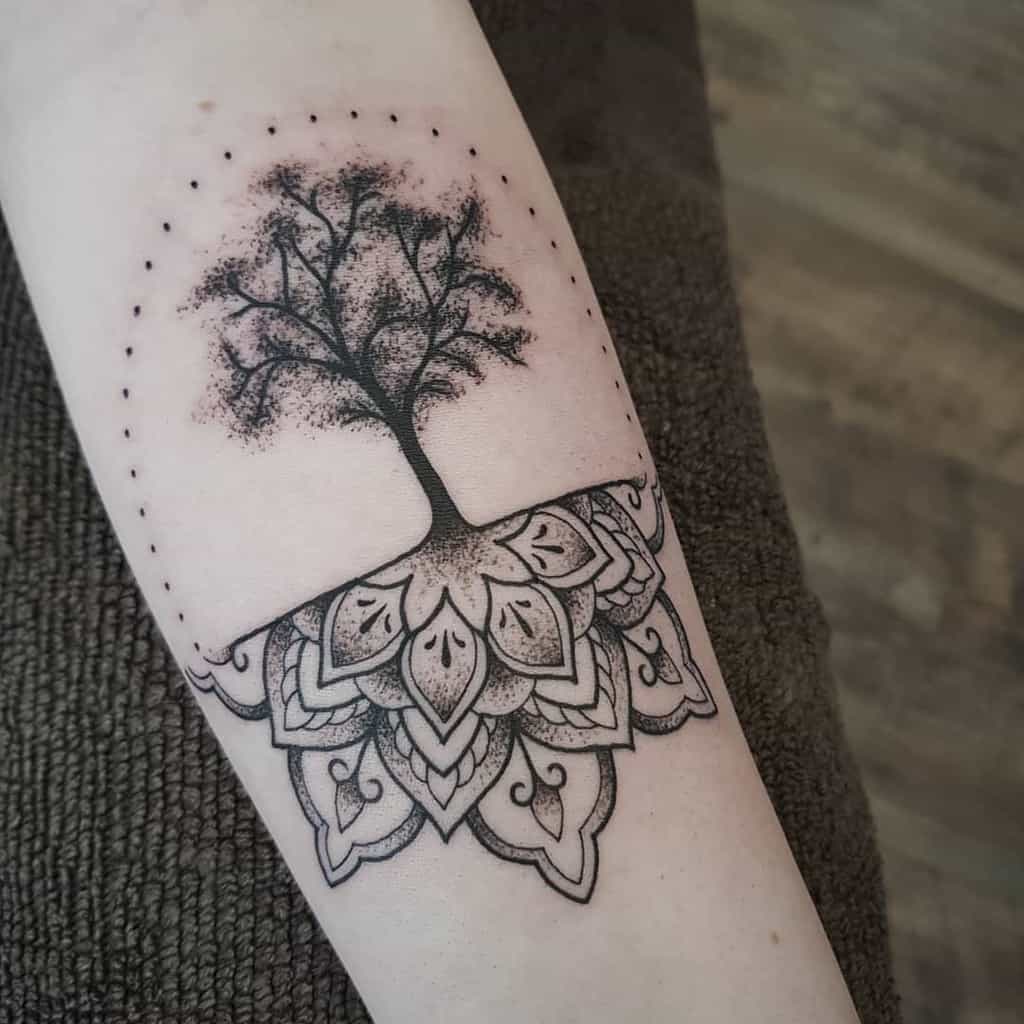 Tattoo of a tree with roots forming a mandala pattern on a person's forearm