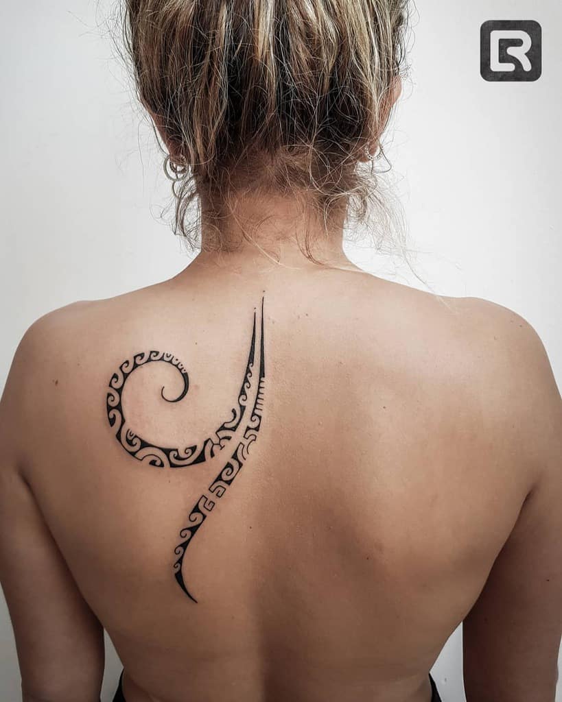 A woman with a stylized tribal tattoo on her upper back, featuring swirling and pointed designs