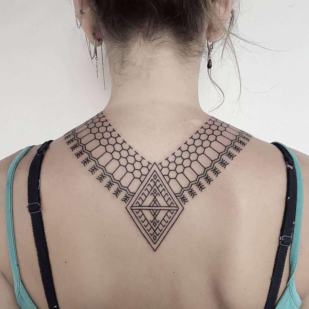 Geometric tattoo on a woman's upper back, featuring hexagonal and diamond patterns with intricate linework