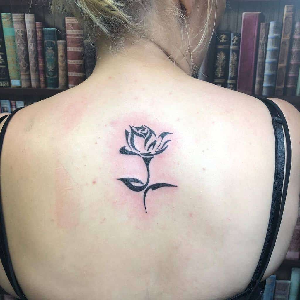 Black rose tattoo with tribal patterns on a woman's upper back
