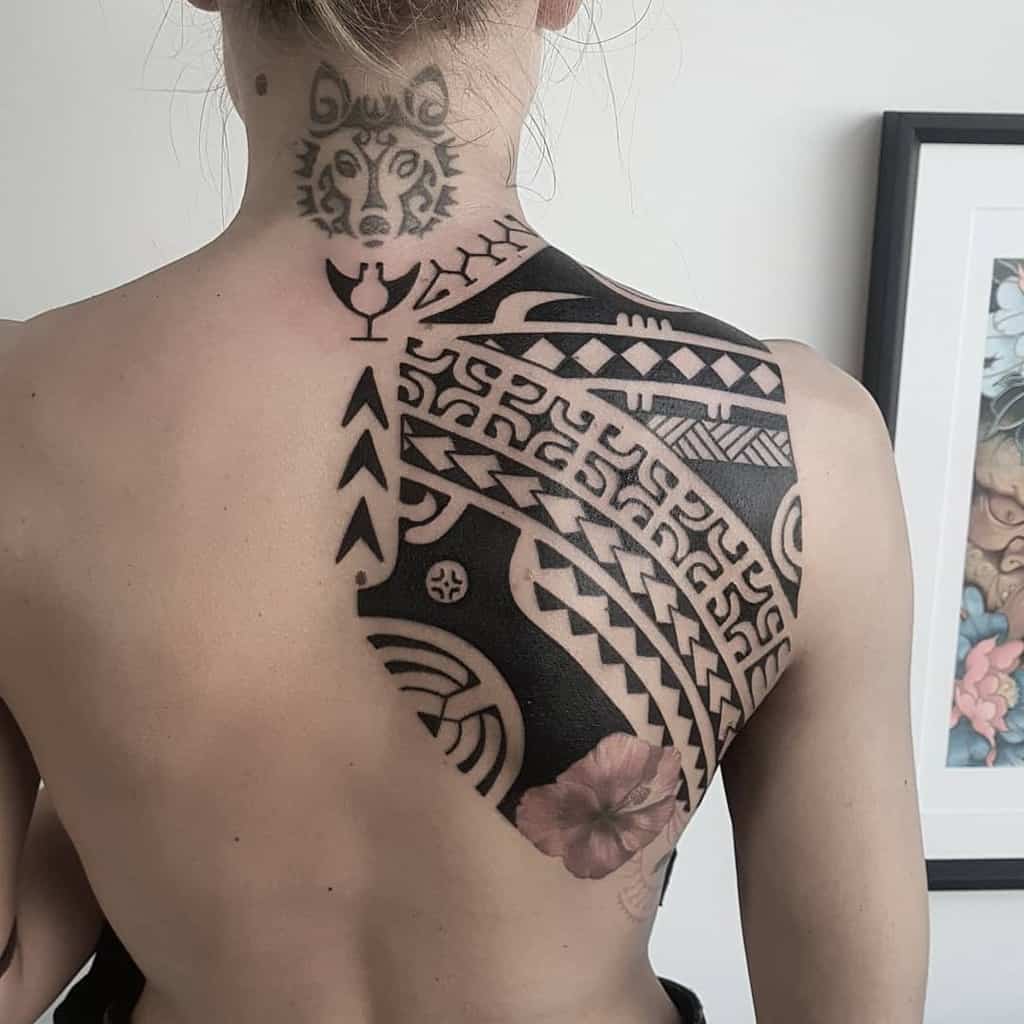 Woman with intricate geometric and nature-themed tattoos on her upper back 