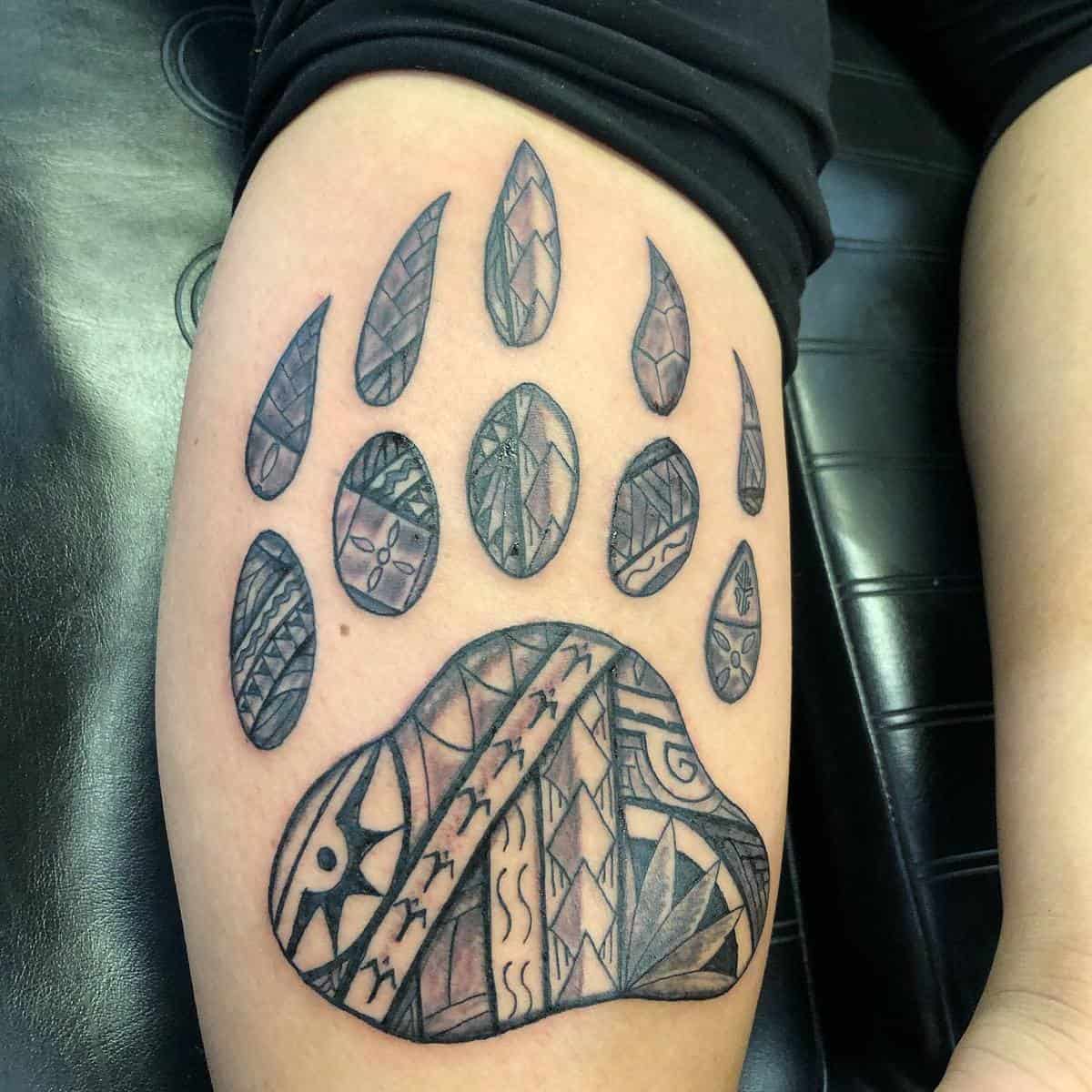 Tattoo of a stylized bear paw with tribal patterns on a person's arm