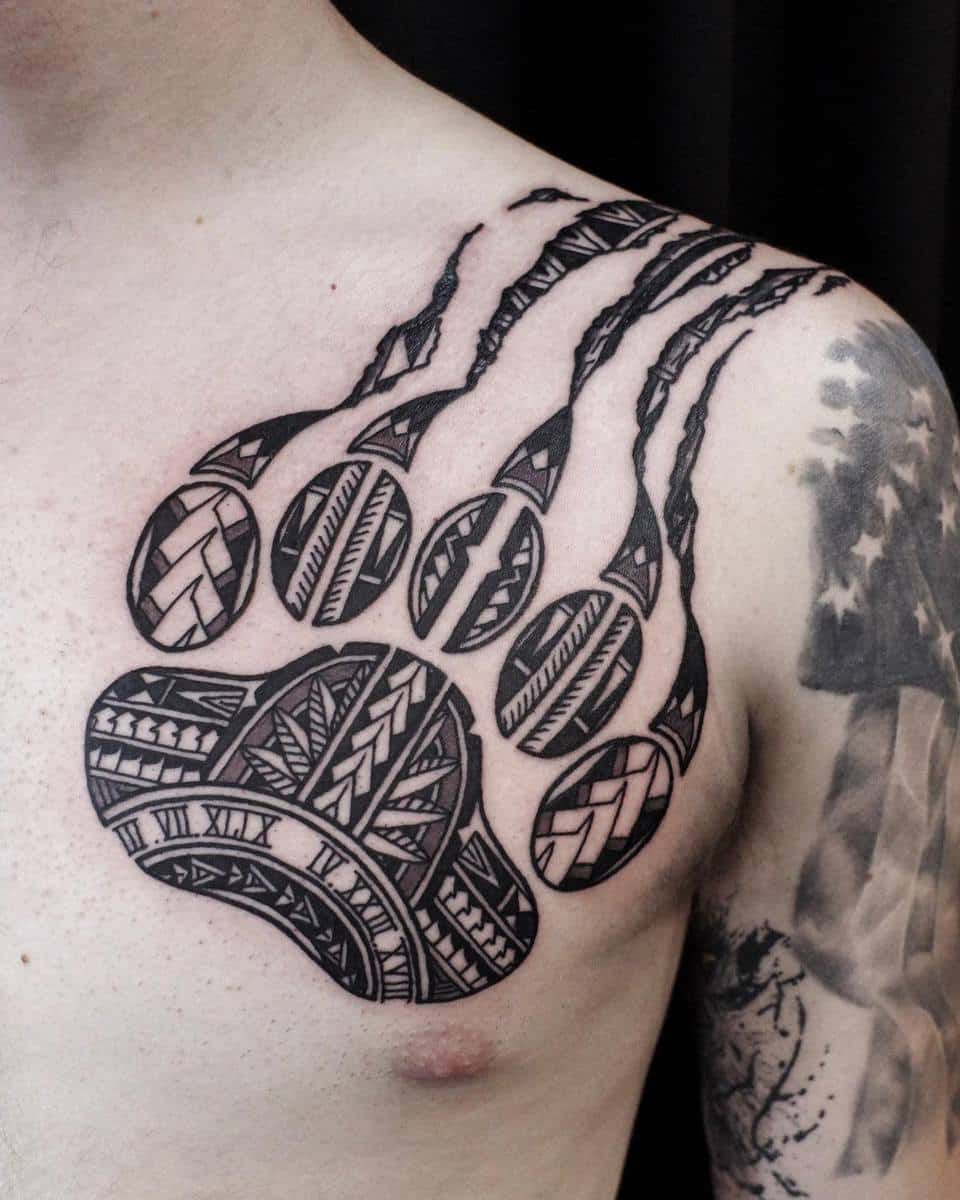 Tattoo of a bear paw with tribal patterns on a person's shoulder and upper chest