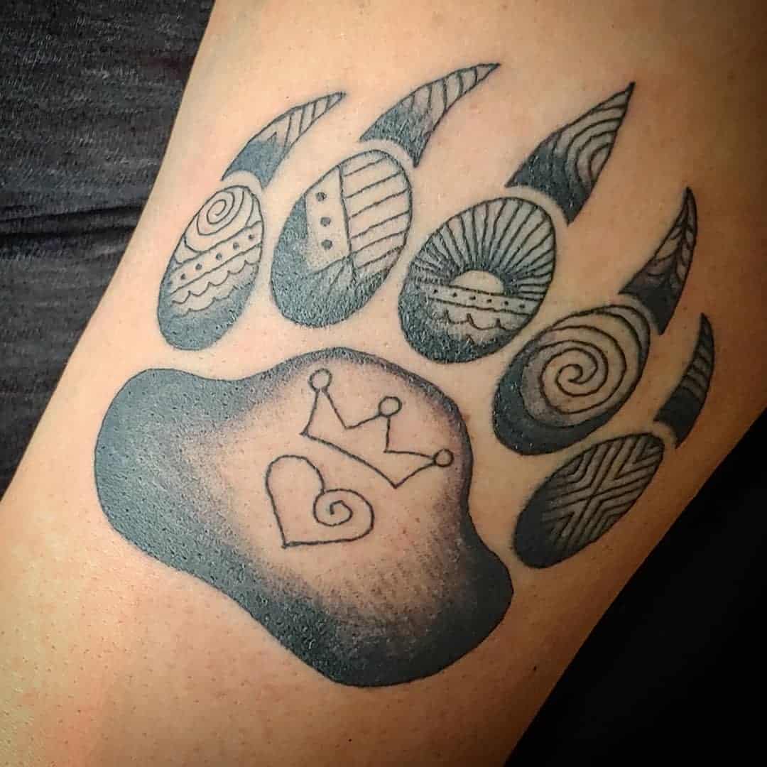 Tattoo of a bear paw print with patterns and a crown inside a heart on the largest pad