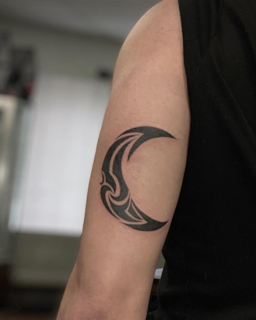 Arm with a crescent moon tattoo etched in a striking tribal style