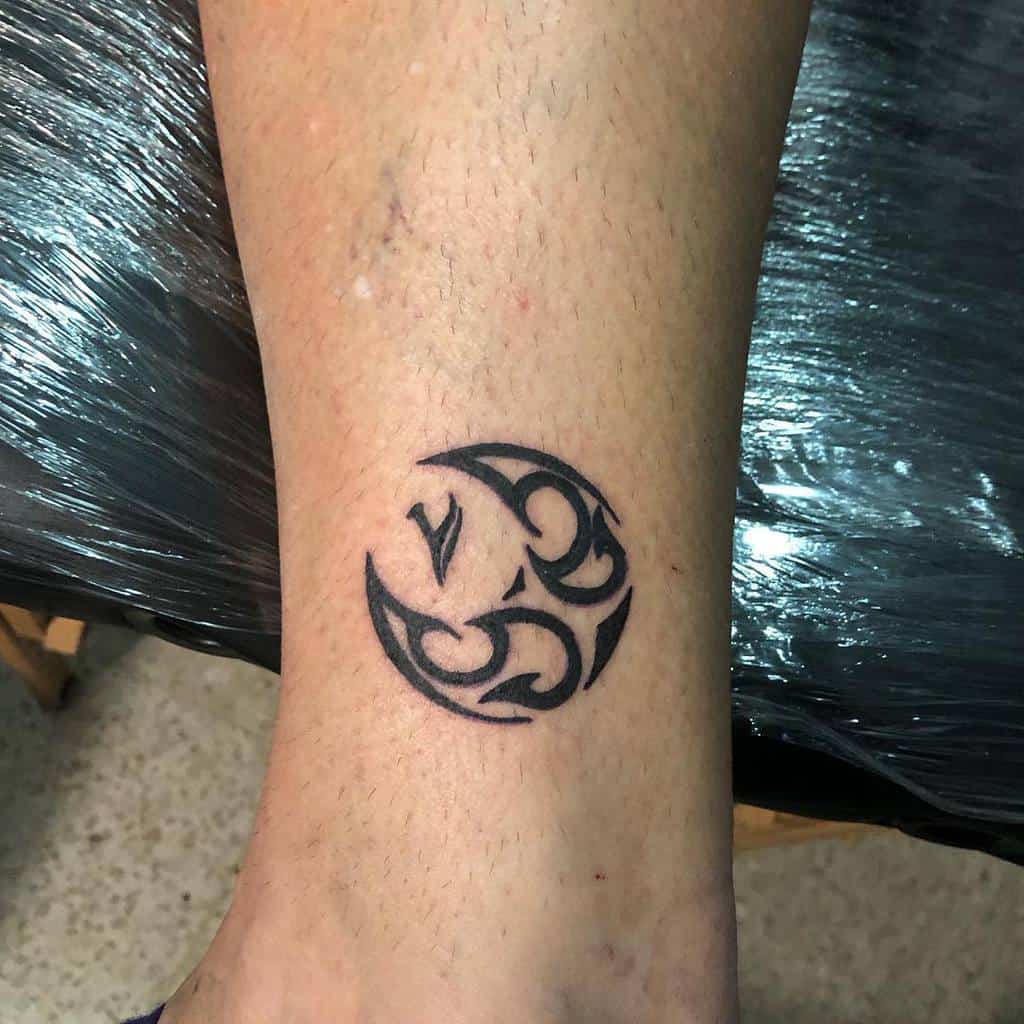 Black tribal-style tattoo in circular design on an ankle