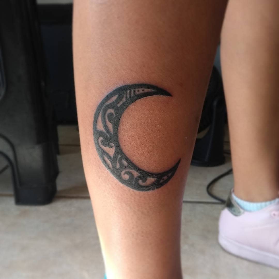 Tattoo of a crescent moon with tribal patterns on leg