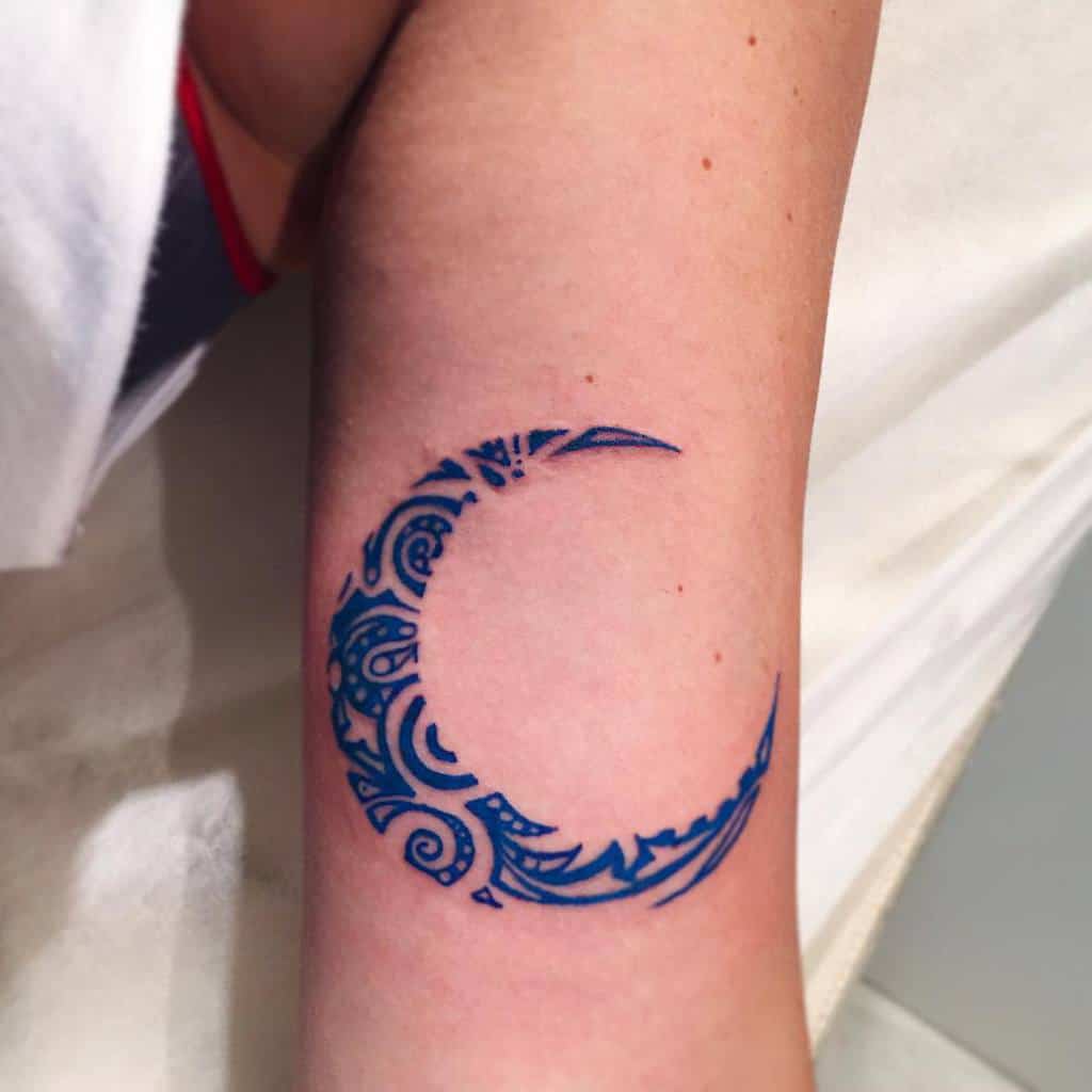 A blue crescent moon tattoo with intricate patterns on a person's forearm