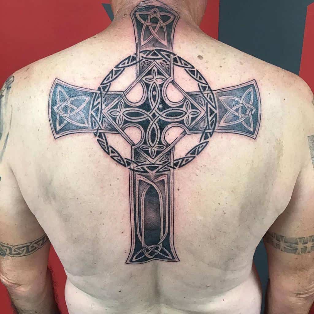 A back tattoo featuring an imposing Celtic cross adorned with intricate knotwork and geometric patterns