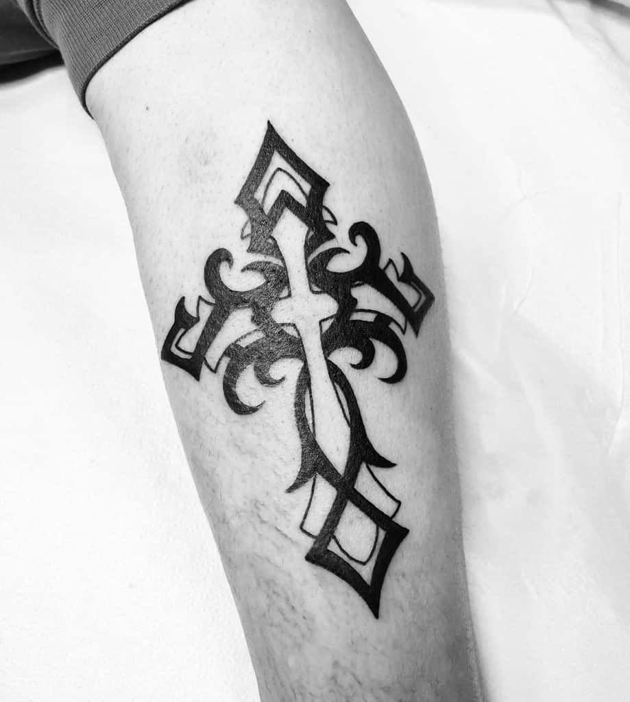 A striking black tribal cross tattoo graces the forearm
